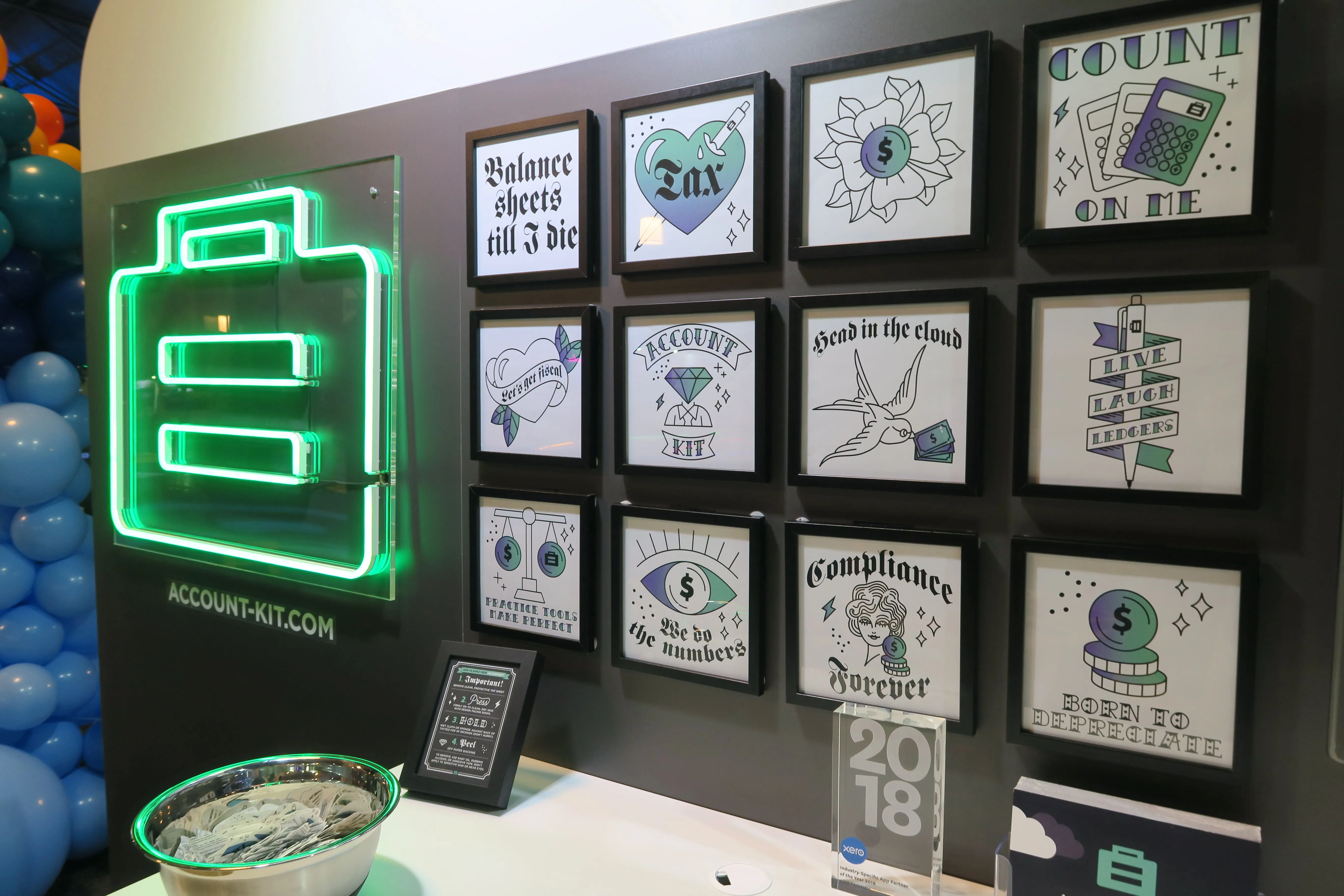AccountKit’s tattoo parlour stand at Xerocon, with a neon AccountKit logo and framed accounting-pun tattoo designs