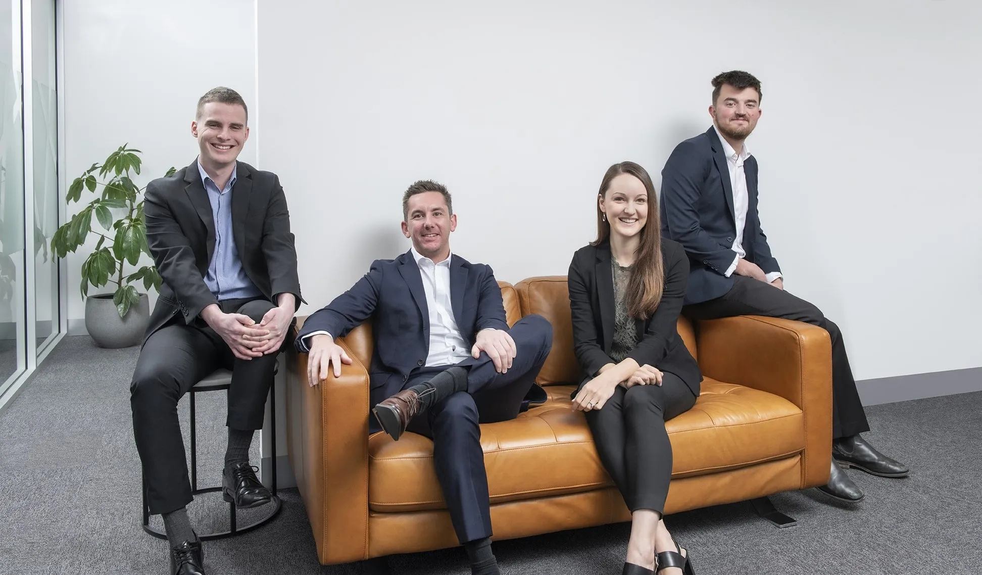 The four-person Stafford Accounting team seated on and around a tan leather sofa